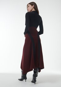 Lange bordeauxrode rok met zwarte paneelaccenten, gemaakt van een gestructureerde stof. Gecombineerd met kniehoge zwarte laarzen en een aansluitend zwart topje.