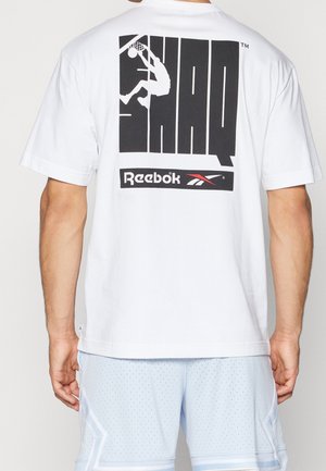 Biała bawełniana koszulka z krótkim rękawem, z dużą czarną grafiką "SHAQ" oraz logo "Reebok" na plecach, o luźnym fasonie.