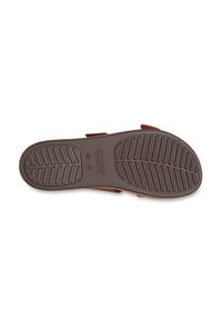 Brown rubber shoe sole with textured grip pattern, featuring a raised logo and markings for size. Accented with adjustable straps.