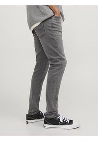 Jeans slim fit grises con una textura suave, diseño de cinco bolsillos y sutilezas en las costuras. Combinados con zapatillas negras con suelas blancas.