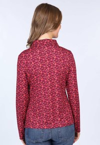 Long-sleeve top in dark pink fabric with a floral pattern in shades of orange and purple, featuring a collar and fitted design.