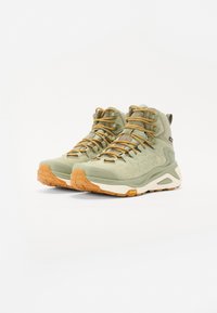 Bocanci de drumeție impermeabili verzi, din suede texturat, cu șireturi maro și talpă Vibram. Au guler căptușit și detalii cu logo pe lateral.