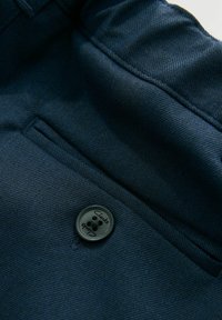 Marineblaue Stoff mit strukturiertem Gewebe, ausgestattet mit einem runden schwarzen Knopf mit dem Text "Clarks" und einem gestickten Taschendetail.