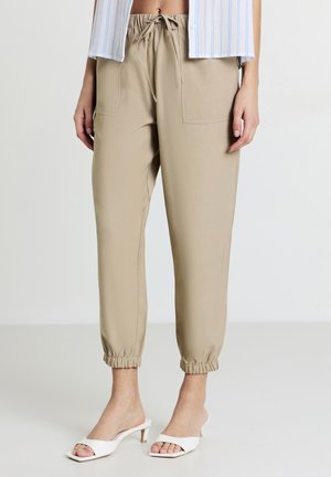 Helle beige Hose mit elastischem Taillenbund und Bündchen, ausgestattet mit zwei Vordertaschen und einer glatten Stoffoberfläche.