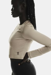 Haut cropped beige à manches longues avec un col rond, design ajusté et détail logo sur l'ourlet. Assorti avec des leggings noirs taille haute.