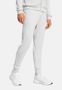 Hellgraue sportliche Sweatpants aus einem weichen Stoff, mit Seitentaschen, schmal zulaufenden Beinen und kontrastierenden Nähten. Kombiniert mit weißen Sneakern.