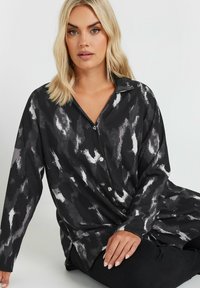 Black and white patterned button-up shirt with a collar, textured fabric, and long sleeves, featuring a relaxed fit and side slits.