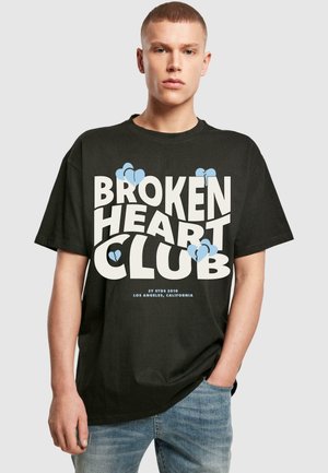 Sort bomulds T-shirt med fed hvid tekst "BROKEN HEART CLUB" og blå hjerte grafik. Løs pasform og korte ærmer, afslappet design.