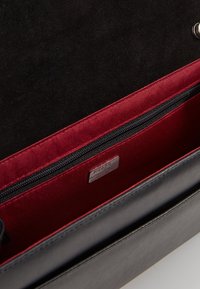 Zwarte leren tas interieur met rood satijnen voering, ritsvak en zilveren merklabel. Zachte textuur met gestructureerd ontwerp.