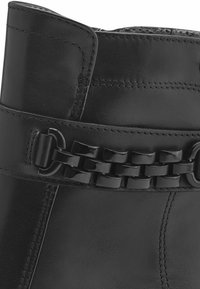 Botín negro de cuero hasta el tobillo con una correa texturizada y detalle de cadena. Acabado suave con costuras visibles. Diseño estructurado.