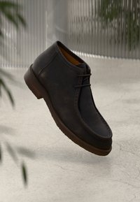 Stivali alla caviglia in pelle marrone con punta rotonda, dettagli di cucitura discreti e design con lacci. Suola leggera con finitura testurizzata.