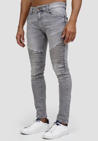 Jeans skinny grigi con un look strappato, caratterizzati da dettagli a coste sulle cosce. Realizzati in denim, progettati per una vestibilità aderente. Abbinati a sneakers bianche.