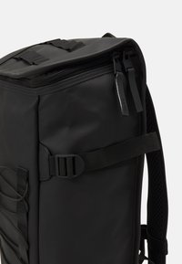 Svart ryggsekk laget av vanntett materiale, med glidelås, justerbare stropper, spenner og mesh-detaljer på bakpanelet.