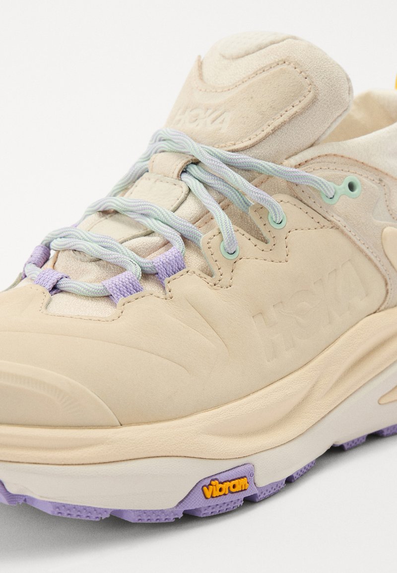 Beżowe sneakersy z teksturowaną zamszową i siateczkową cholewką, z pastelowymi sznurowadłami i podeszwą Vibram. Wytłoczone logo i kolorowe akcenty w pobliżu podeszwy.