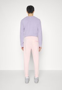 Fialová dlouhá rukávová blůza v kombinaci s světle růžovými tepláky. Tepláky mají zadní kapsu a celkový outfit doplňují šedé sportovní tenisky.