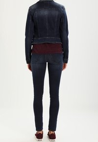 Tmavě modrá džínová bunda s krátkým střihem, doplněná o mramorovou texturovanou halenku a tmavé skinny džíny. Obuv tvoří vínové tenisky.