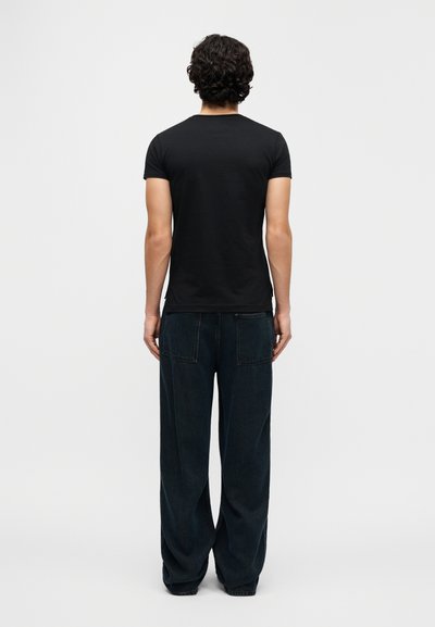 Camiseta negra de manga corta combinada con pantalones de mezclilla oscuros de pierna ancha, con un ajuste relajado y diseño minimalista, vista desde atrás.