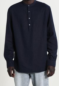 Camicia a maniche lunghe blu navy con colletto rotondo, apertura a tre bottoni e vestibilità leggermente rilassata, realizzata in tessuto testurizzato.