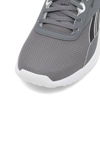 Szary but sportowy z teksturowaną siateczkową cholewką, zaokrąglonym noskiem, białą podeszwą i szarymi sznurowadłami. Po bokach czarne akcenty.