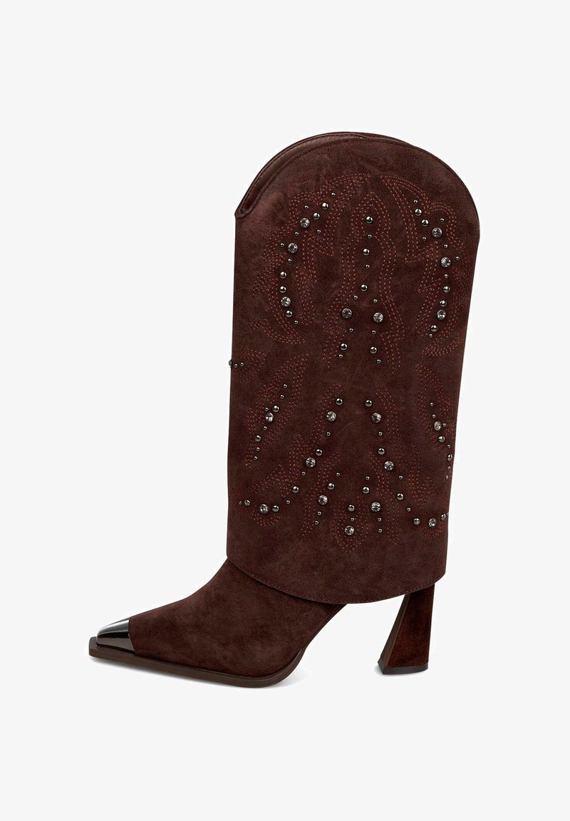 Brązowy zamszowy but z wydłużonym, zaokrąglonym mankietem i spiczastym czubkiem. Posiada dekoracyjne przeszycia i ćwieki. Masywna pięta z metalowym akcentem.