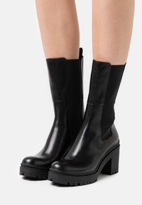 Black leather ankle boots with elastic side panels, chunky heels, and rugged rubber soles, featuring a smooth finish and minimal detailing.