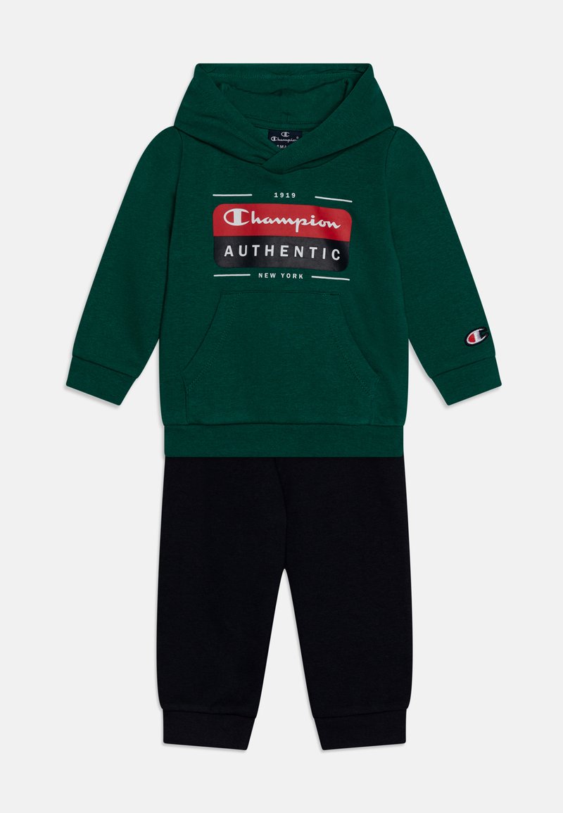 Sudadera verde con un bolsillo frontal, que presenta un logotipo impreso. Combinada con pantalones de chándal negros, ambos confeccionados en una tela suave con puños elásticos.