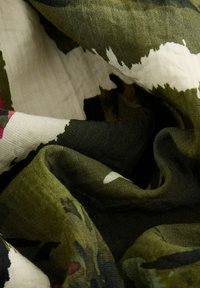 Zielony materiał w wzory, łączący elementy kamuflażu i kwiatowe, z teksturą lekkiego lnu i subtelnymi wariacjami kolorów.