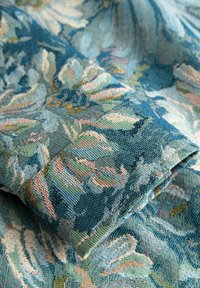 Primo piano di tessuto blu testurizzato con motivo floreale multicolore, che mostra l'intreccio dettagliato e i disegni delle foglie.