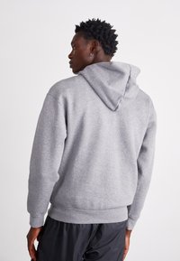 Szürke kapucnis pulóver puha anyagból, húzózsinórral, bordázott mandzsettákkal és hem. Kissé oversized hatású, sima textúrával és minták nélkül.