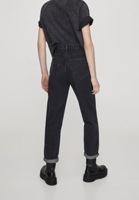 Jean en denim noir à coupe décontractée, ourlets retroussés et deux poches arrière. Associé à une chemise courte à manches courtes de couleur foncée.