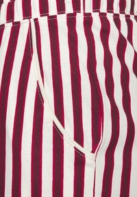 Close-up van stof met verticale rode en witte strepen, met een zijzak en stiksels van de elastische tailleband.