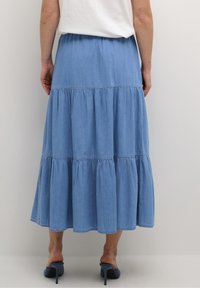 Ljust blå, lagerad denimkjol med elastisk midja som når mitt på vaden. Har gathered sömmar och en flödande siluett.