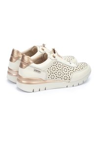 Zapatillas deportivas blancas con un diseño perforado, detalles en oro rosa metálico y una suela acolchada. Presentan un estilo fácil de poner con cordones.
