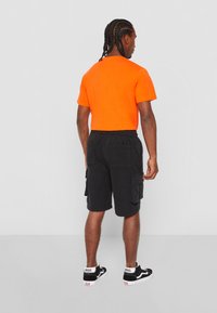 T-shirt orange à manches courtes associé à un short cargo noir avec poches latérales et une coupe décontractée, complété par des baskets Vans noires.