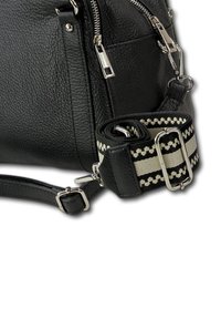 Zwarte leren handtas met een gestructureerd oppervlak, zilverkleurige beslagdelen en een afneembare zwart-cream gestreepte schouderriem.