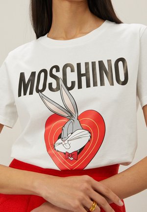 Biały t-shirt z napisem „MOSCHINO”, z postacią Króliczka Bugsa w czerwonej muszce wewnątrz ilustracji czerwonego serca.