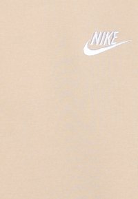 Tricou bej din bumbac, cu un logo Nike brodat alb pe pieptul stâng. Textură netedă, cu o croială normală.