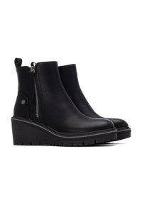 Botas de tobillo de cuero negro con tacón de cuña, cremallera lateral y tira de agarre. Textura suave con detalles de costura sutiles.