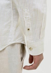 Camisa de rayas de colores claros con puños abotonados y una tela suave y texturizada. Las rayas son sutiles y en una paleta de colores neutros.