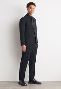 Black tailored suit made of smooth fabric, featuring a single-button jacket, matching trousers, and polished black dress shoes.