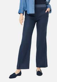 Marineblaue weite Hosen aus leichtem Stoff mit einem elastischen Bund. Kombiniert mit dunkelblauen Wildleder-Slippern mit einer Schleifenakzent.