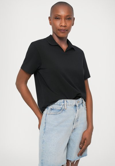 Fekete pamut polóing, lapos gallérral és rövid ujjakkal, világoskék farmer sorttal, koptatott szegéllyel párosítva.