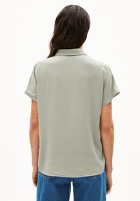 Lichtgroene blouse met korte mouwen, gladde stof, met kraagontwerp, rechte snit en zijsplitten, gecombineerd met blauwe jeans.