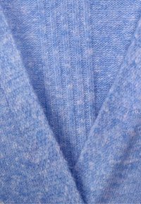 Detailní záběr na měkkou, světle modrou pletenou látku s žebrovaným vzorem a žmolkovou texturou, ukazující překrývající se vrstvy.