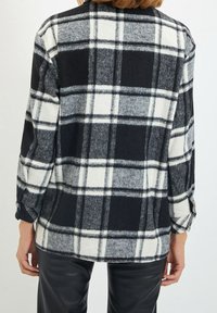Camicia a quadri bianca e nera in un tessuto morbido e testurizzato. Maniche lunghe, polsini con bottoni e una vestibilità rilassata. La vista posteriore evidenzia il motivo.