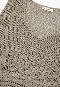 Knit tank top in muted beige with a scoop neck. Features an open weave texture and geometric pattern along the hem. Label: Ole Koton.