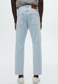Pantalones vaqueros de denim azul claro con un corte relajado, que presentan un parche de cuero marrón en la parte trasera de la cintura y dos bolsillos traseros. Se pueden ver zapatillas blancas.