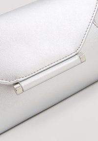 Bolso de mano plateado con acabado texturizado, que cuenta con un cierre de solapa y un elegante asa metálica.