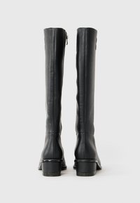Botas de couro pretas até ao joelho com uma textura suave, fecho de zíper lateral e um pequeno salto bloco com um detalhe de marca.