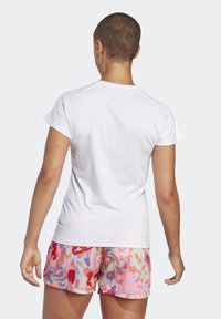 Bílá košile s krátkými rukávy a kulatým výstřihem, doplněná o đa barevné kraťasy s rů žovými, modrými a červenými akcenty.